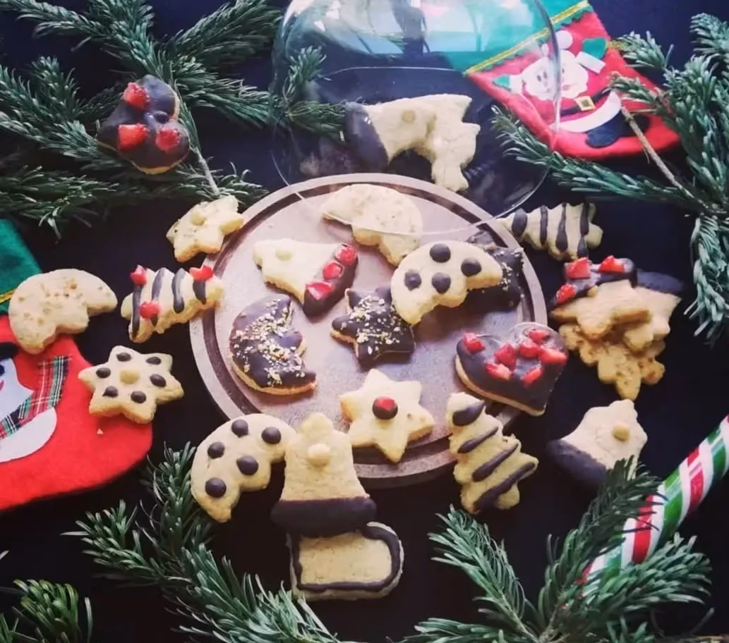 Une assiette est déposée sur des branches de sapin, elle contient quelques petits sablés aux formes originales et d'autres sont dispersés autour.