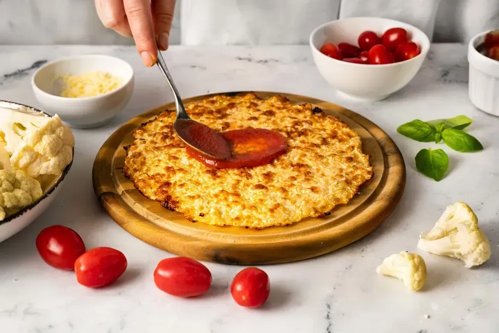 After this four-seasons pizza is baked, a person holding a spoon puts tomato sauce on the pizza.