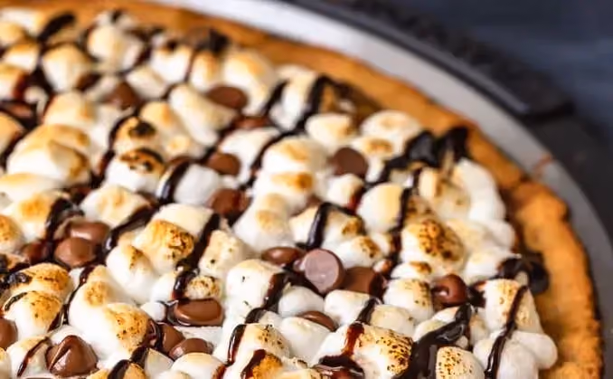 Encore dans son plat de cuisson, la pizza est recouverte de chocolat avec les marshmallows disposés avec application pour le plus bel effet visuel.