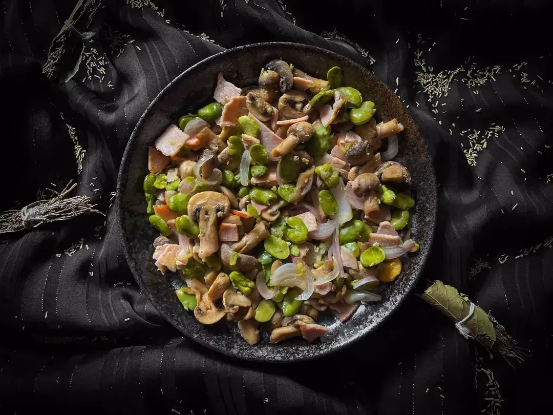 The pan-fried broad beans, button mushrooms, and bacon are presented in a small blue bowl.