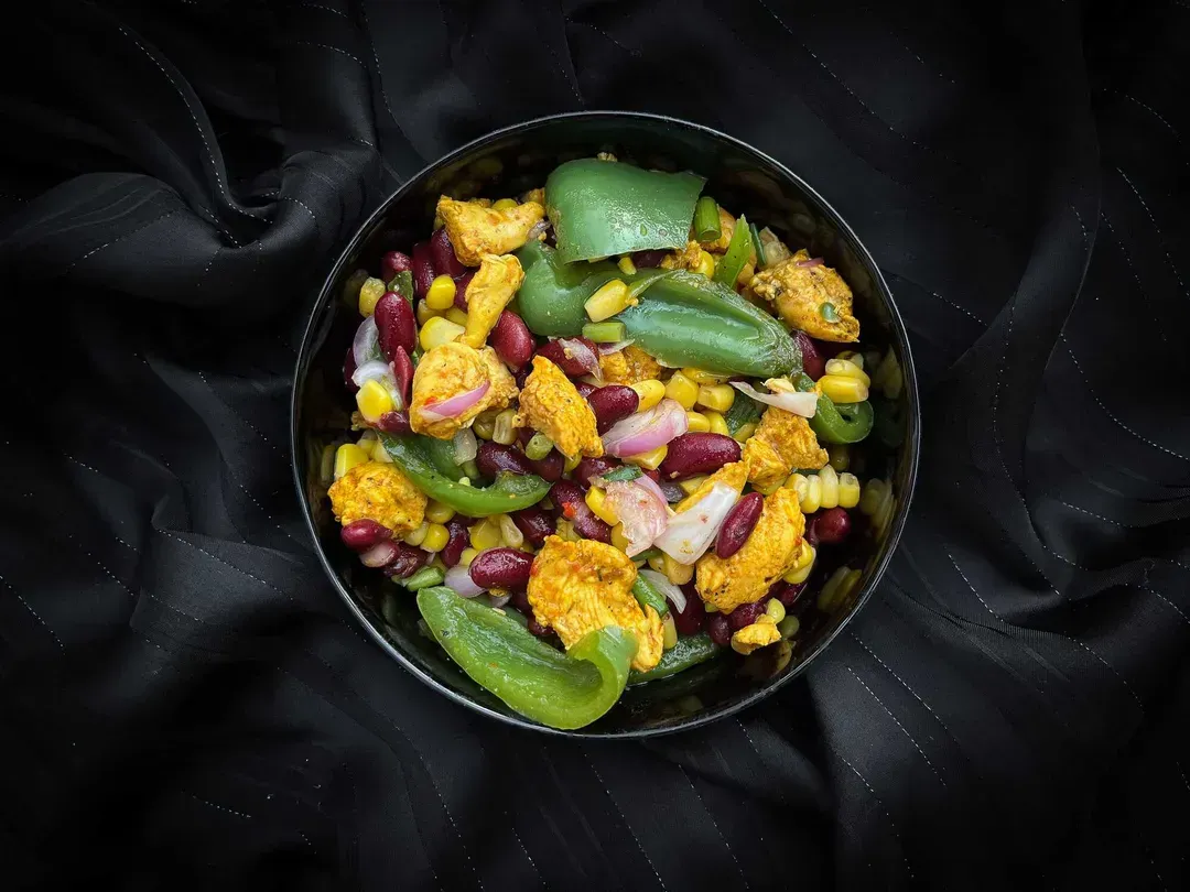 In a medium-sized bowl, there is chicken accompanied by red beans, corn, and green bell pepper.