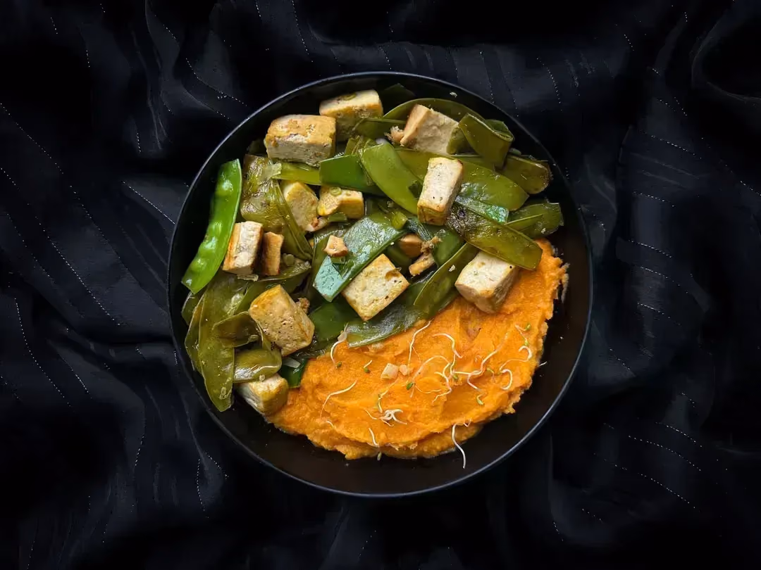 Cette recette très colorée, une poêlée de tofu, haricots plats et patate douce est présentée dans un petit saladier de couleur bleu.