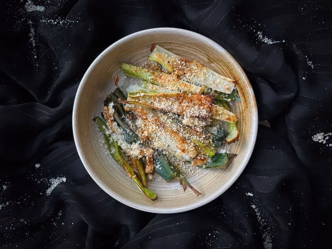 Les poireaux gratinés au parmesan sont présentés dans un petit saladier en grès de couleur beige.