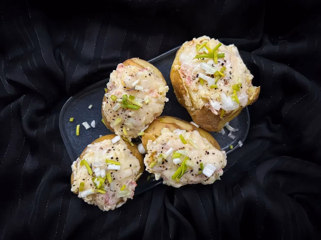 In a rather rustic setting, three large stuffed potatoes are placed on a shallow wooden dish.