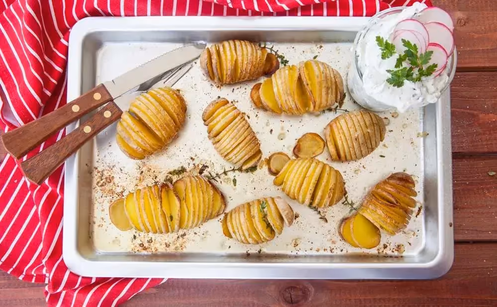 Set on a red-and-white striped kitchen towel is a dish filled with halved potatoes sliced into thin rounds