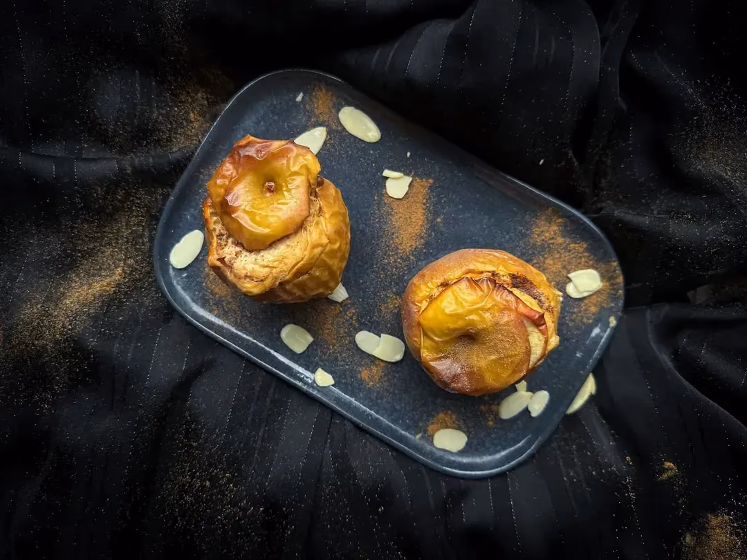 Deux pommes au four et crème vanillée protéinée sont présentée sur un plat rectangulaire en faïence peu profond de couleur bleu.