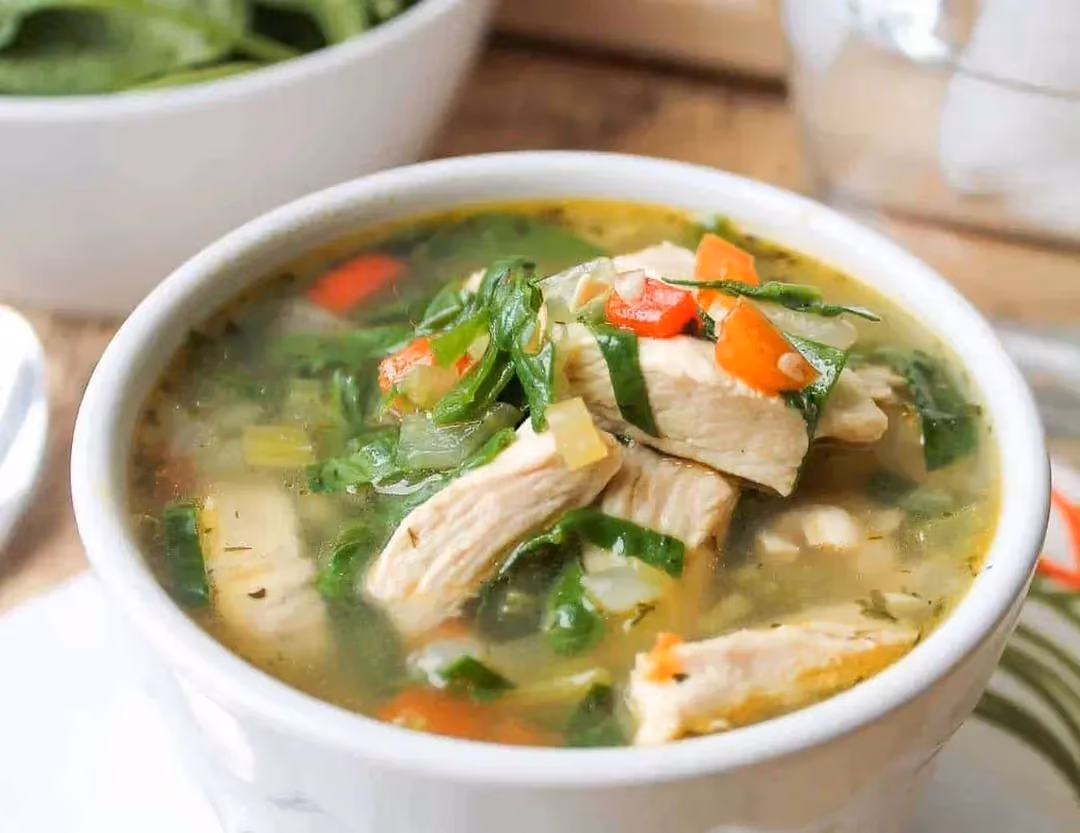 De gros morceaux de poulet accompagnés d'épinards composent ce potage au poulet présenté dans un grand et large bol en faïence de couleur blanc.