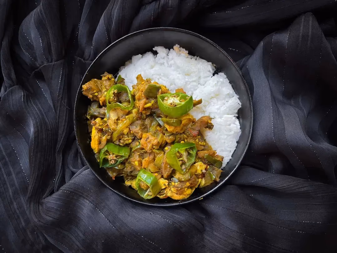 La recette de poulet, bringelles et gros piments est présentée dans un petit saladier de couleur bleu.