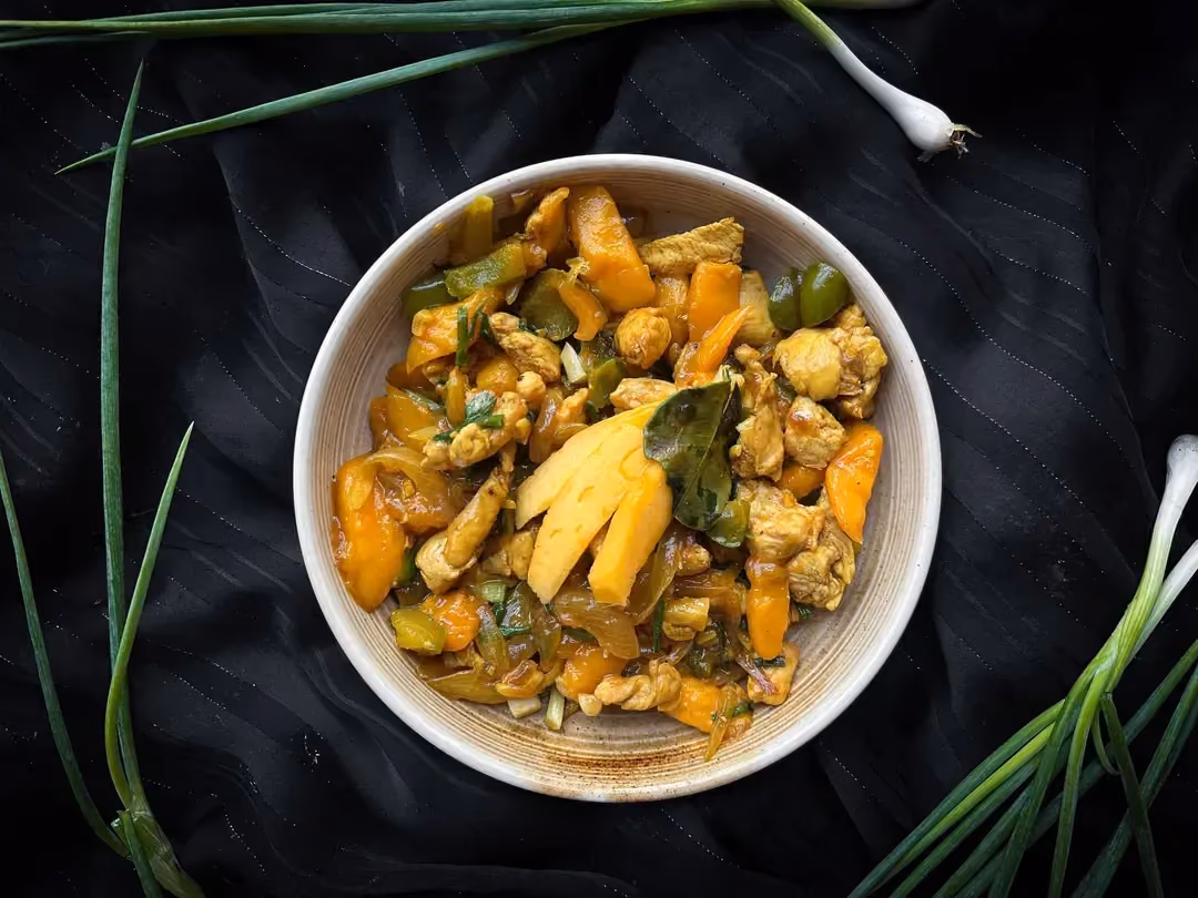 Dans un grand bol de couleur bleu, se trouve le poulet accompagné avec du riz. Sur la table une mangue sans sa peau est prédécoupée en petits dés.