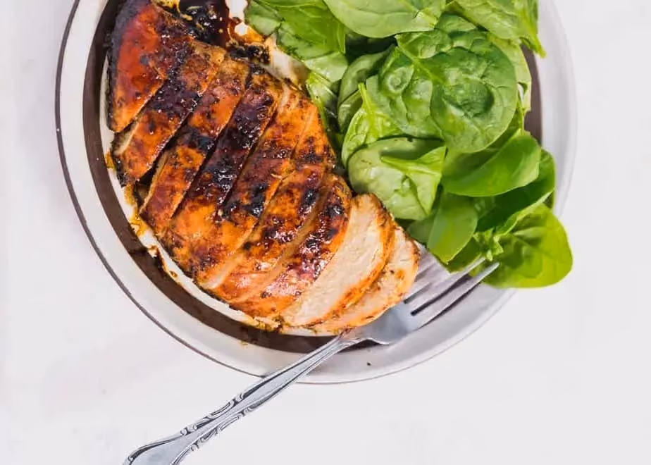 Dans un plat se trouve de grosses et belles tranches de poulet grillées et marinées au vinaigre balsamique. Et à côté du poulet de la salade verte.