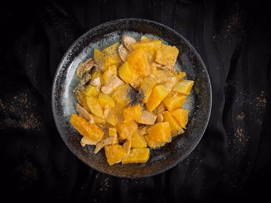 In a small blue bowl are pieces of chicken and butternut squash, brightly colored yellow by the yellow curry.