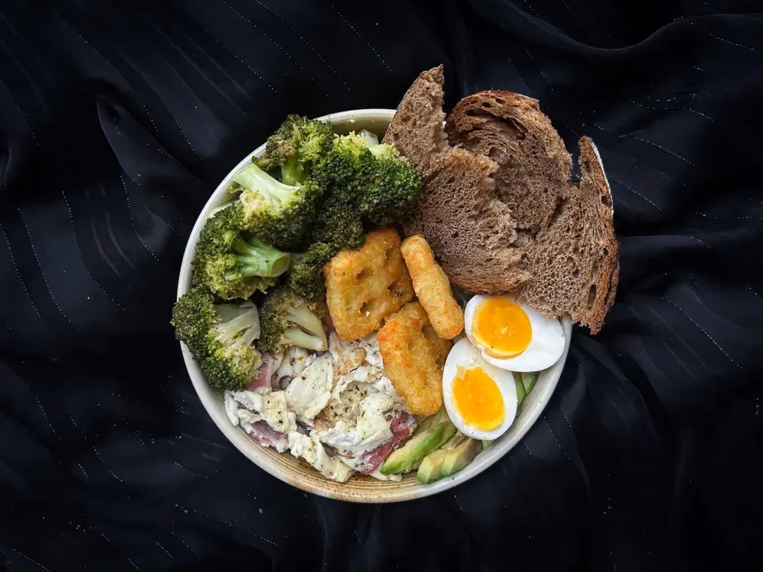 Une assiette contient le Power bowl composé d'oeufs, bacon, brocolis, avocat, ainsi que deux galettes Rostis et une tranche de pain de seigle.