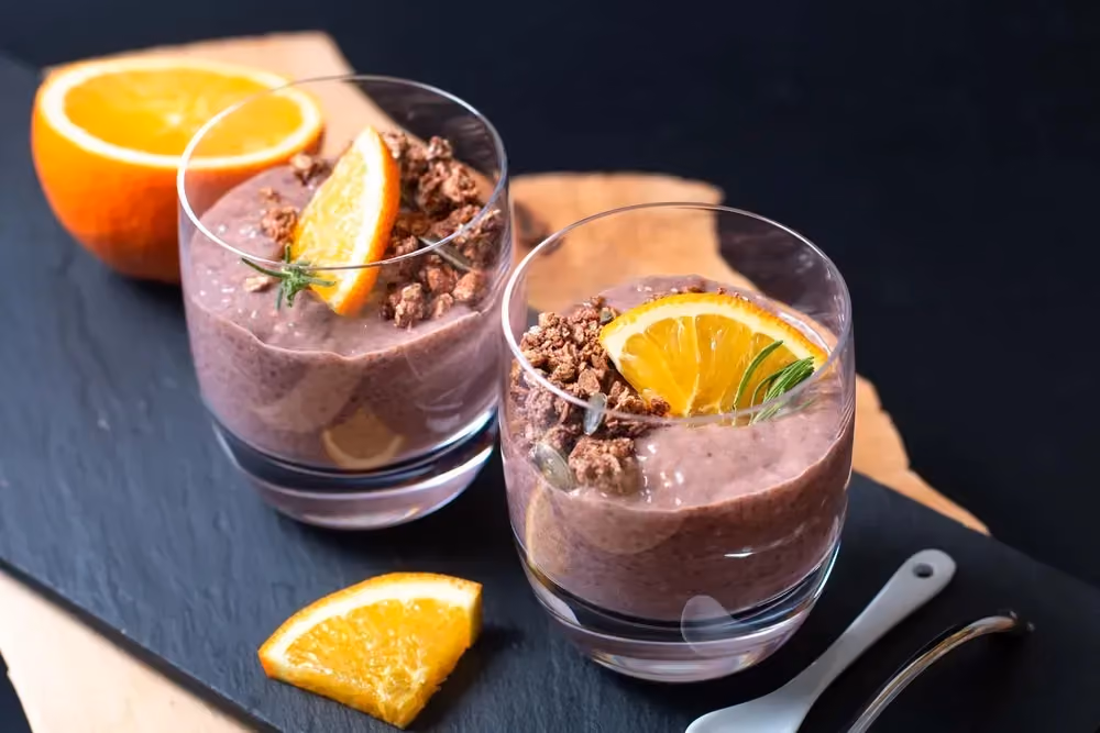 Deux verrines contiennent le pudding au chocolat et graines de chia. Le topping est réalisé avec une fine tranche d'orange dans chaque verrine.