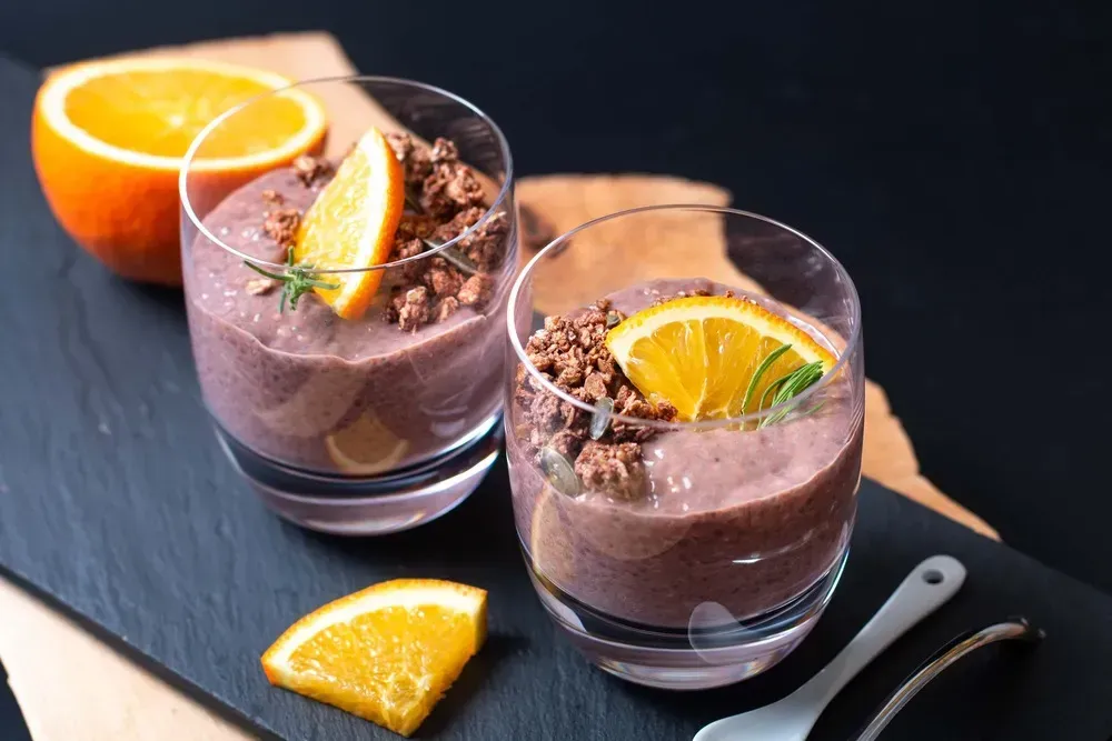Two glass cups contain chocolate chia pudding. The topping is made with a thin slice of orange in each cup.