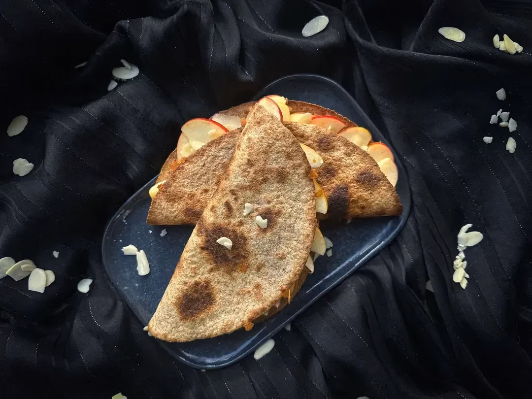 Two quesadillas with apples, shredded mozzarella, and almonds are arranged on a shallow rectangular blue plate.