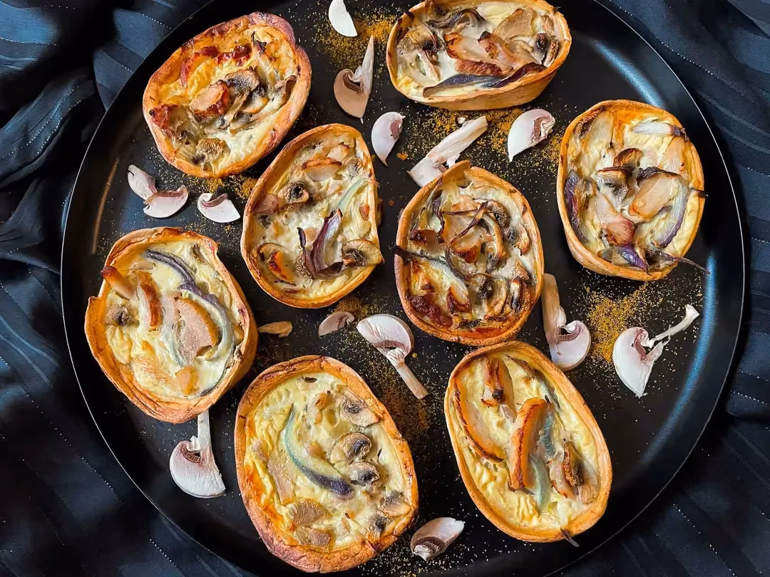 Sur un plat peu profond sont disposées huit petites quiches barquitas parfaitement colorées. Des champignons finement émincés sont disposés deçi-delà.