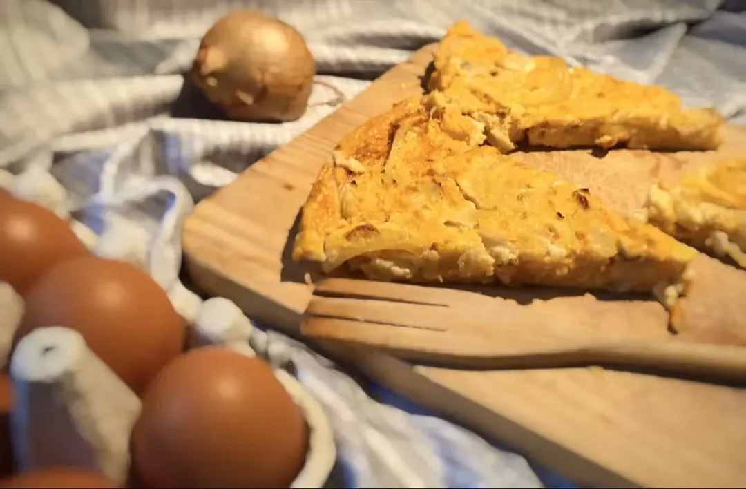 Next to a few eggs, on a wooden board and beside a wooden fork as well, there are pieces of pumpkin and chicken quiche.