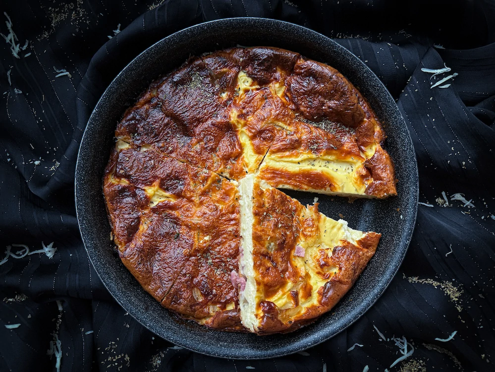 Dans un plat à tarte de couleur blanc, la quiche lorraine sans pâte se présente à nous bien dorée.