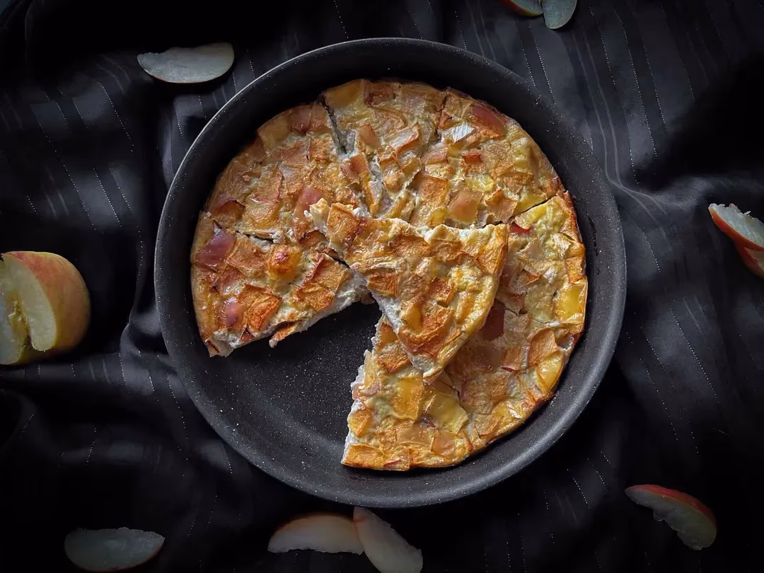 The crustless apple and Camembert quiche is presented in its baking dish. A halved apple sits beside it.