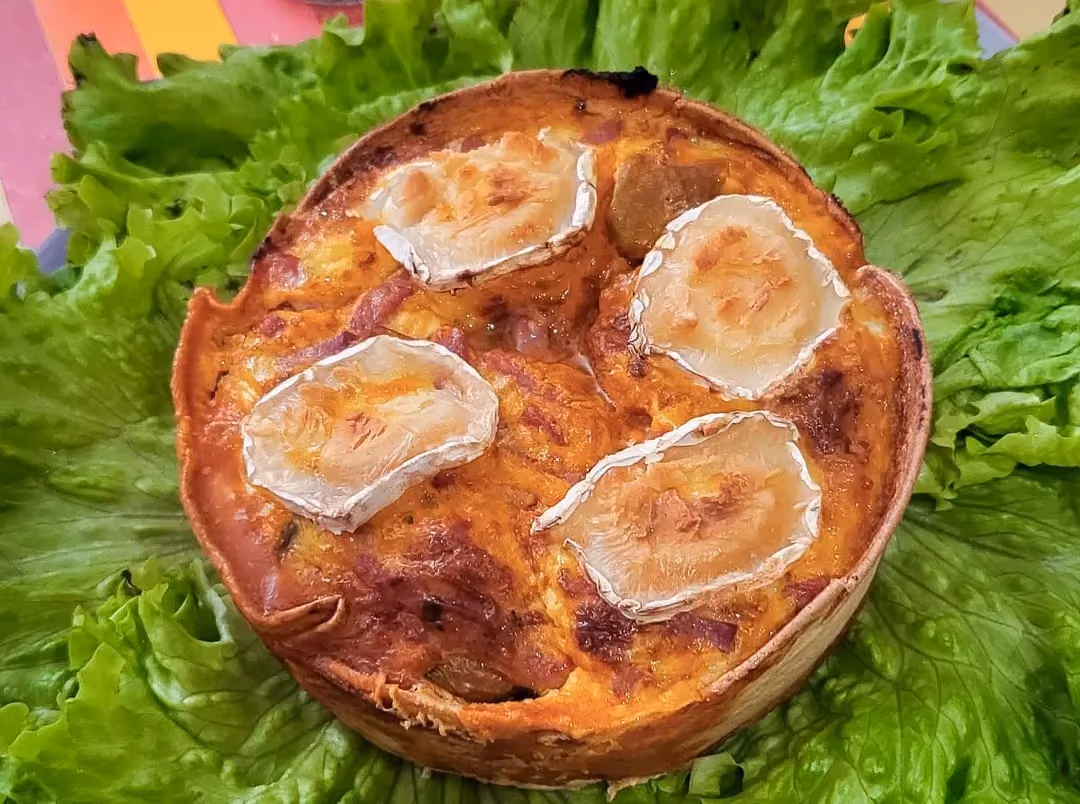 On a bed of green salad, a large wrap holds four small quiches with ratatouille, bacon, and goat cheese.