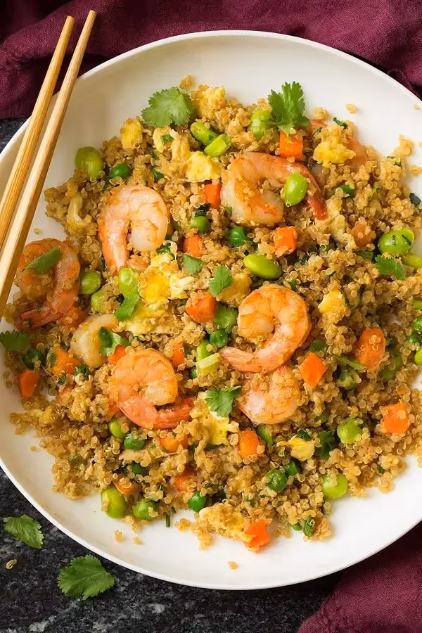In a white bowl, there is fried quinoa along with fully peeled shrimp.
