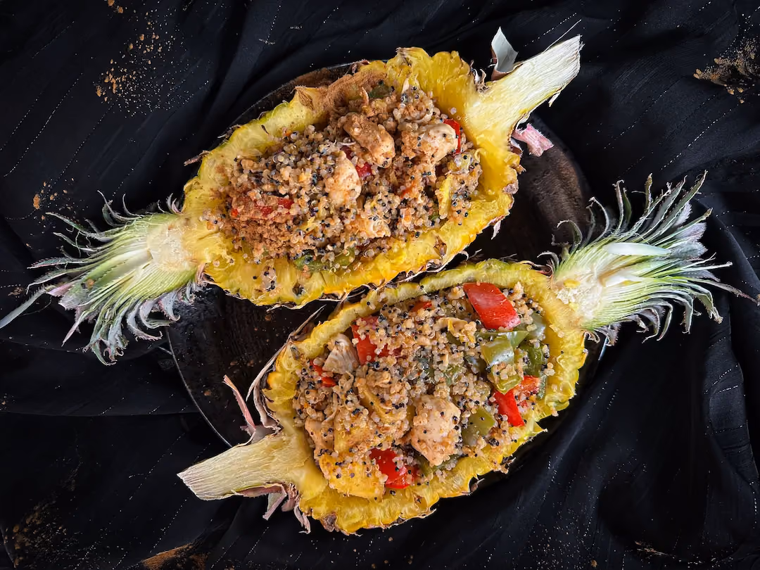 Sur une assiette se trouve un ananas ouvert en deux dans le sens de la hauteur vidé de sa chair. L'ananas sert de réceptacle à la recette.