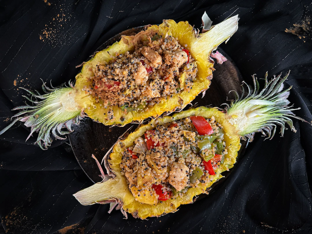 On a plate, there is a pineapple cut open lengthwise and hollowed out. The pineapple serves as the container for the recipe.