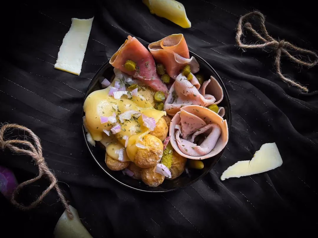 Dans un petit bol se trouve les pommes de terre nouvelles, la viande des Grisons, le jambon fumé et des petites tranches de fromage à raclette.