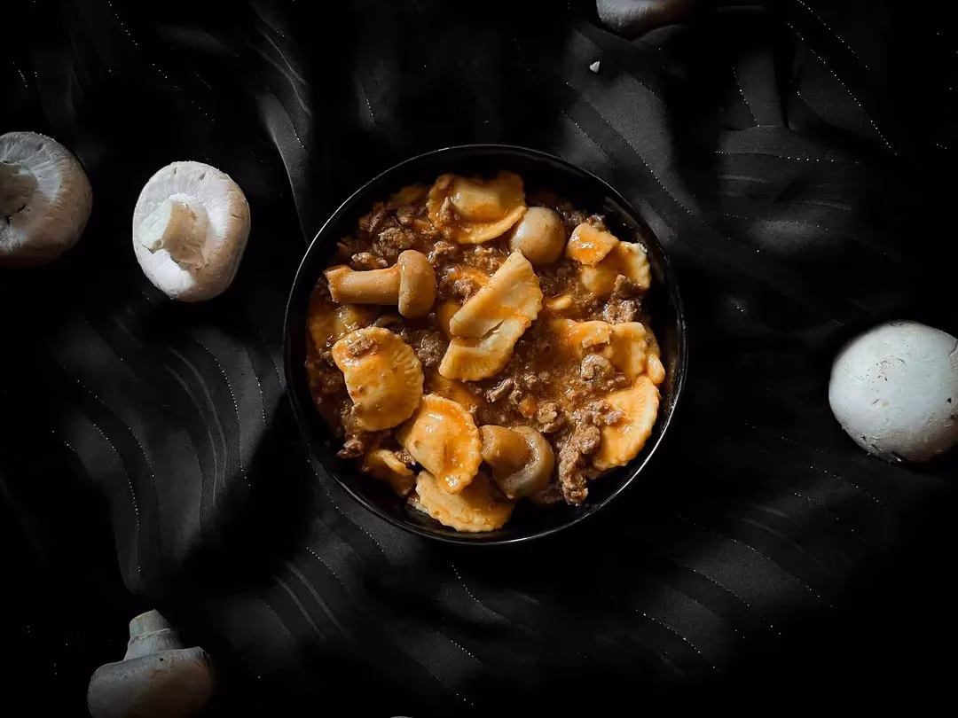 In a small bowl, you can see the ravioli, button mushrooms, and ground meat underneath. Four mushrooms are next to the bowl.