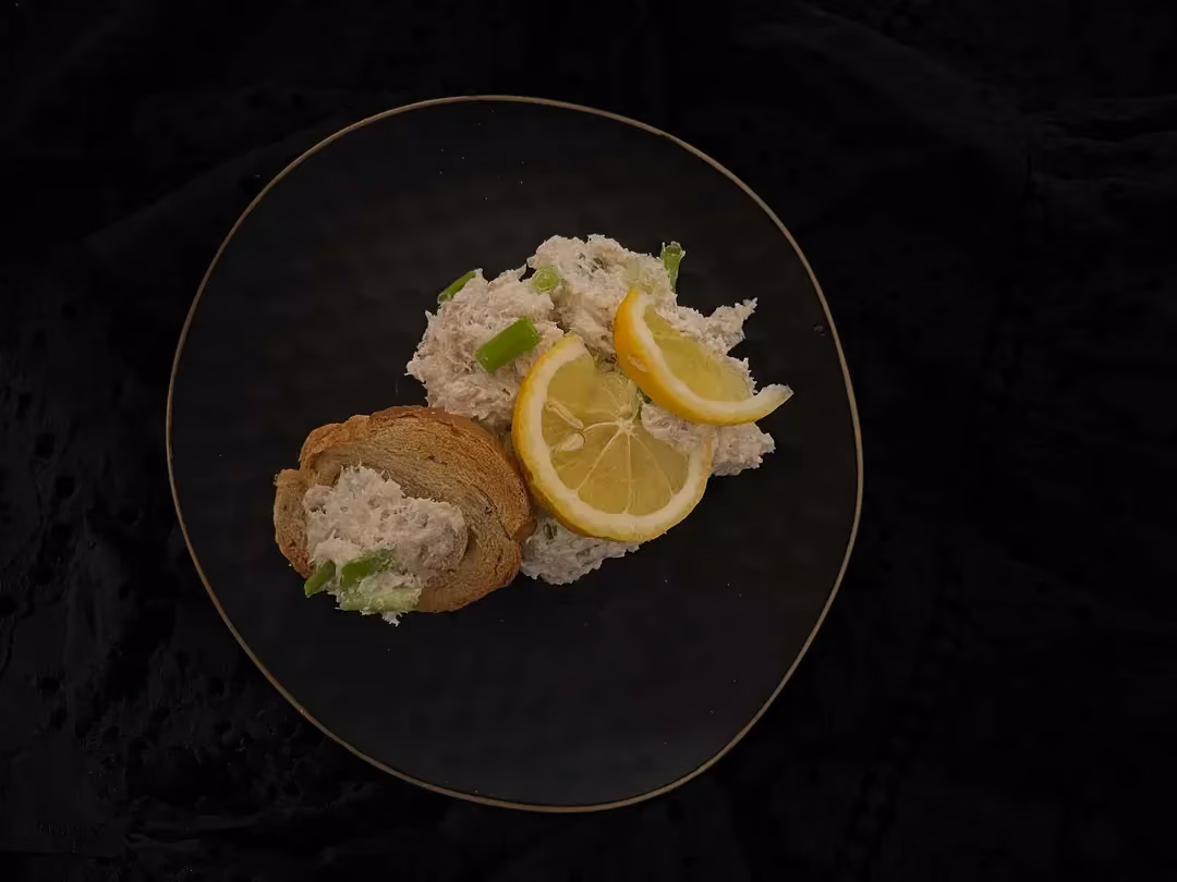 Dans un bol de couleur bleu se trouve les rillettes de cabillaud avec un toast et une tranche fine de citron jaune.