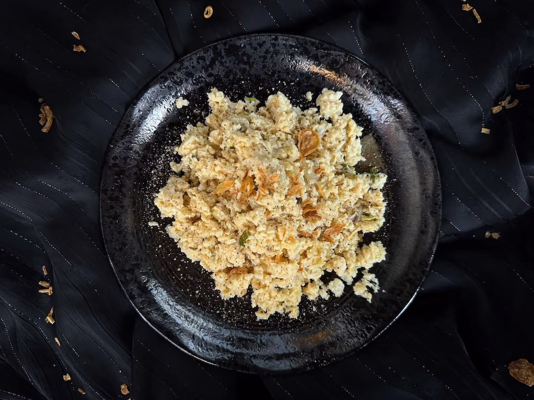 Creamy risotto-style cauliflower sprinkled with parsley, served on a black plate.