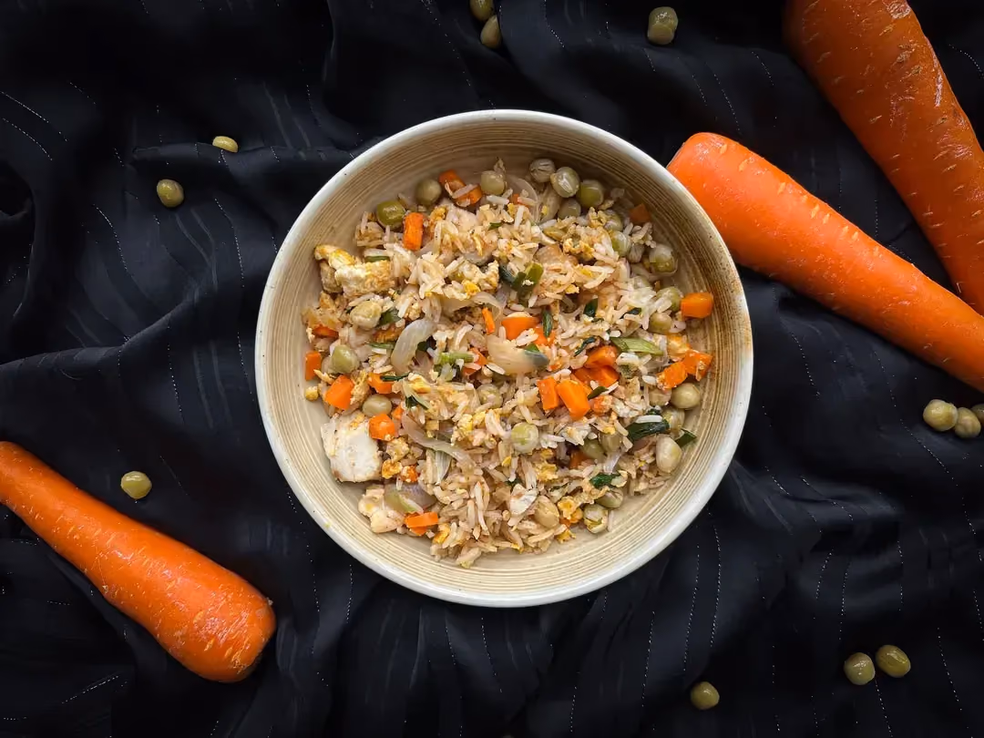 Dans une grande assiette blanche, on retrouve tous les ingrédients du riz cantonais tels que les oeufs, le poulet, les carottes et les petits pois.