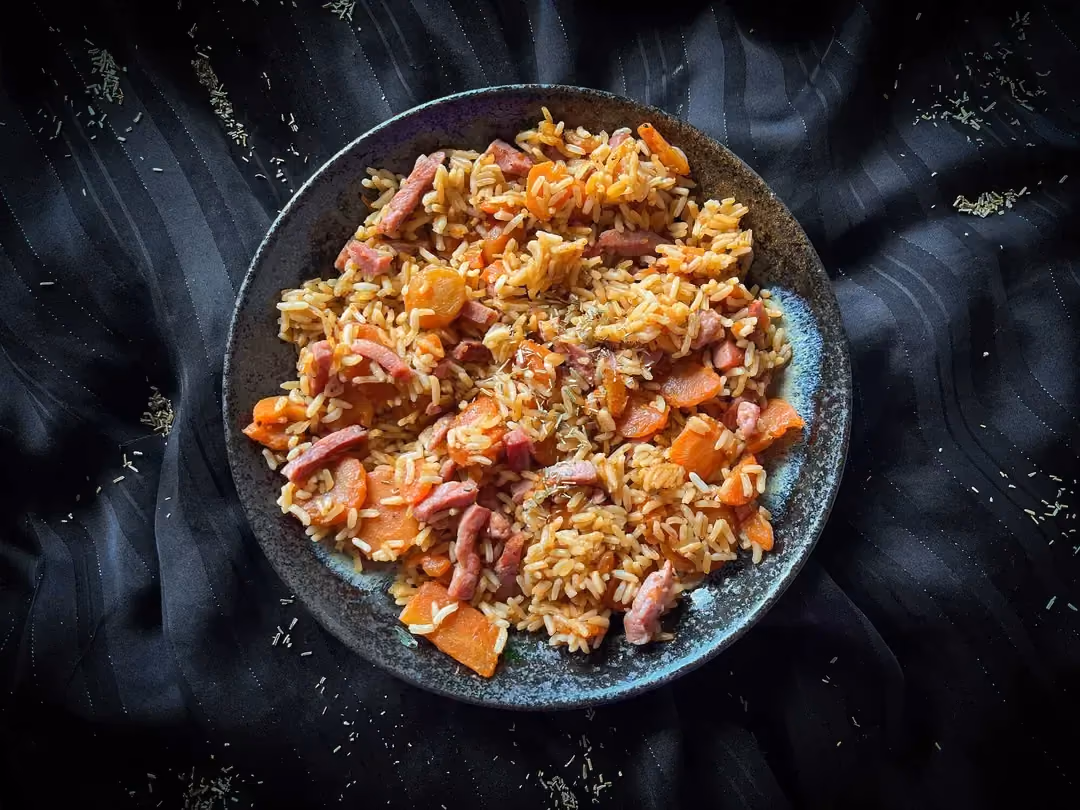 A small blue salad bowl holds the rice recipe with carrots and turkey bacon.