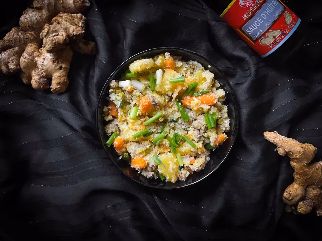 La recette de chou-fleur sauté à l'ananas, boeuf et gingembre est présentée dans un bol. A côté se trouve du gingembre et de la sauce d'huître.