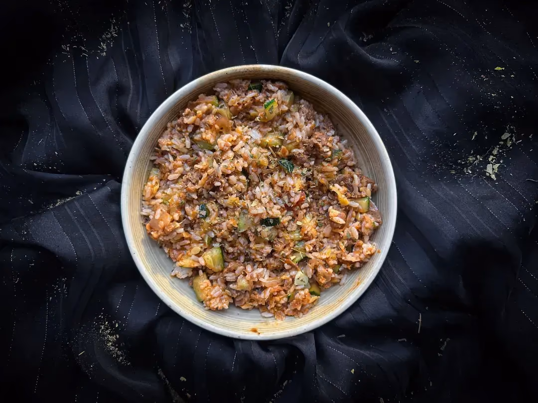A small beige stoneware bowl holds the rice with zucchini, tomato sauce, and plant-based ground meat recipe.
