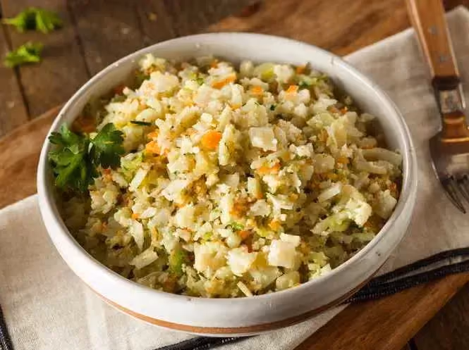 On a towel sits a small earthenware bowl, the cauliflower rice is served with a small bunch of fresh cilantro.