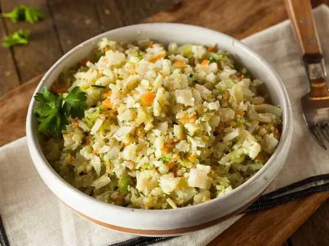 On a towel sits a small earthenware bowl, the cauliflower rice is served with a small bunch of fresh cilantro.
