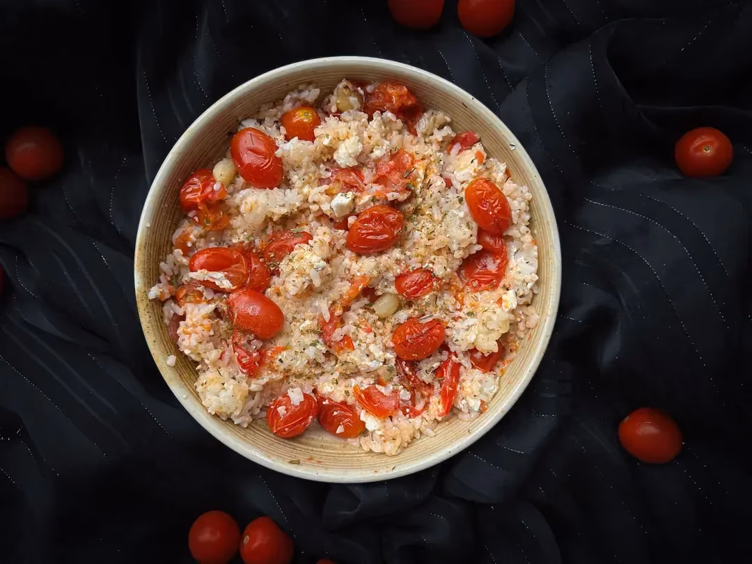 La recette de riz au four aux tomates cerises, feta et ail est présentée dans un petit saladier en grès de couleur beige.
