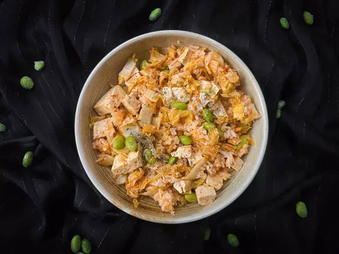 In a small beige stoneware bowl is the recipe for pan-fried rice with red curry, edamame, white cabbage, and tofu.