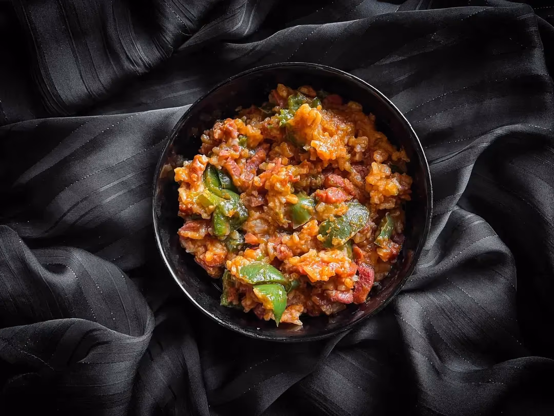 A small bowl holds the rice recipe with tomato sauce, bacon lardons, and bell peppers.