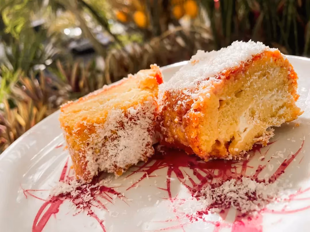 Le roulé est parsemé de noix de coco râpée et il est présenté sur une assiette de couleur blanche décorée à l'aide de colorant alimentaire rouge.
