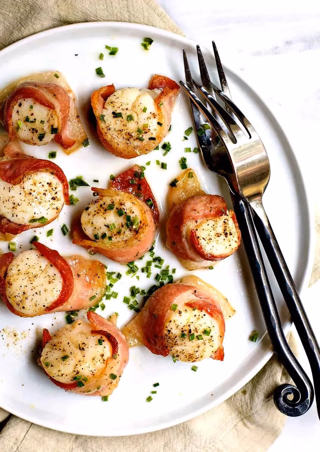 On a white plate, there are eight bacon-wrapped scallop rolls.