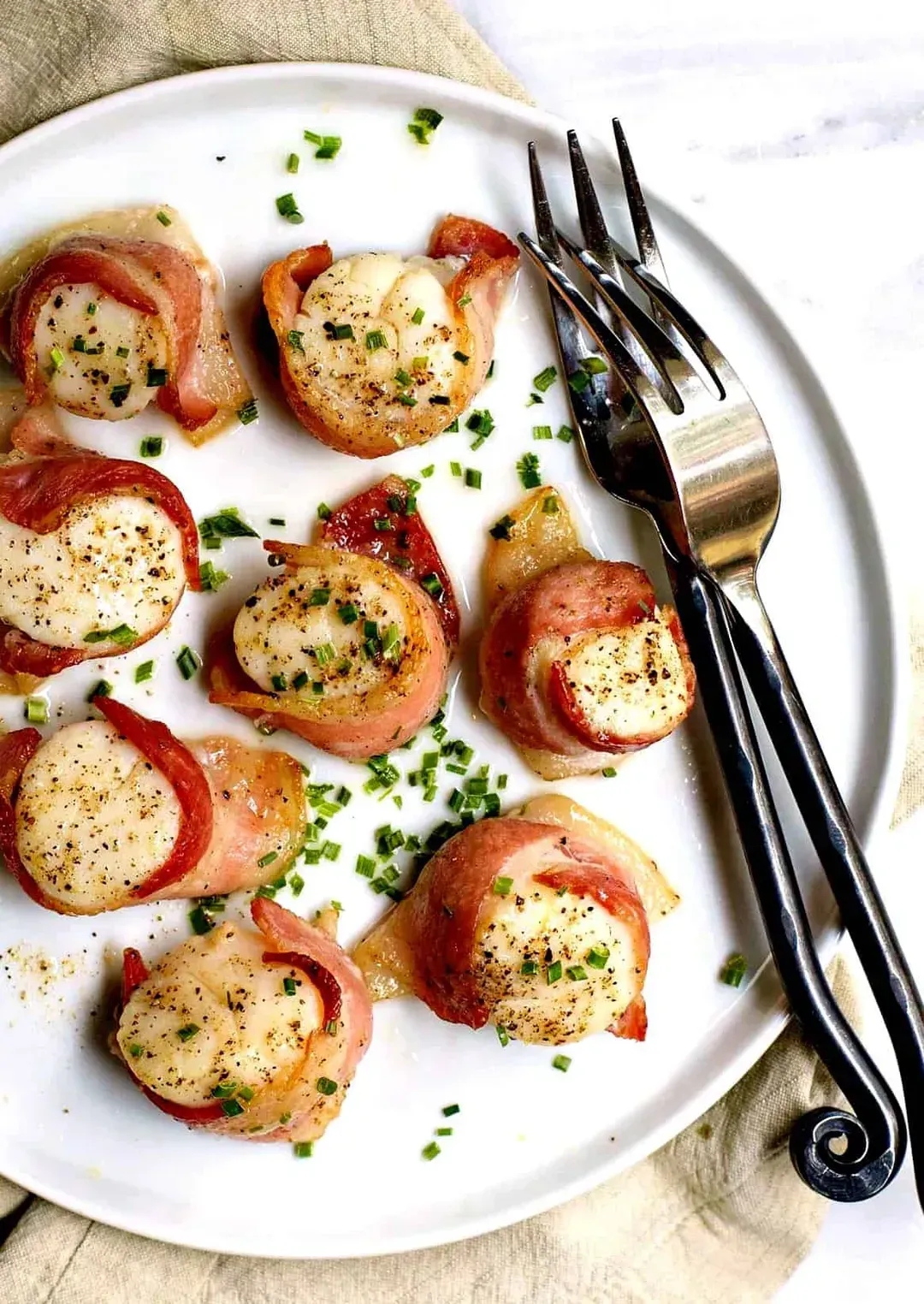 On a white plate, there are eight bacon-wrapped scallop rolls.