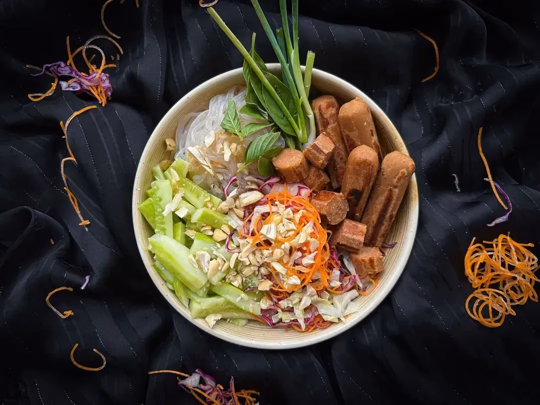 Un petit saladier blanc accueille la salade Bo Bun composée de saucisses végétales coupées en rondelles et de concombres coupés en bâtonnets.