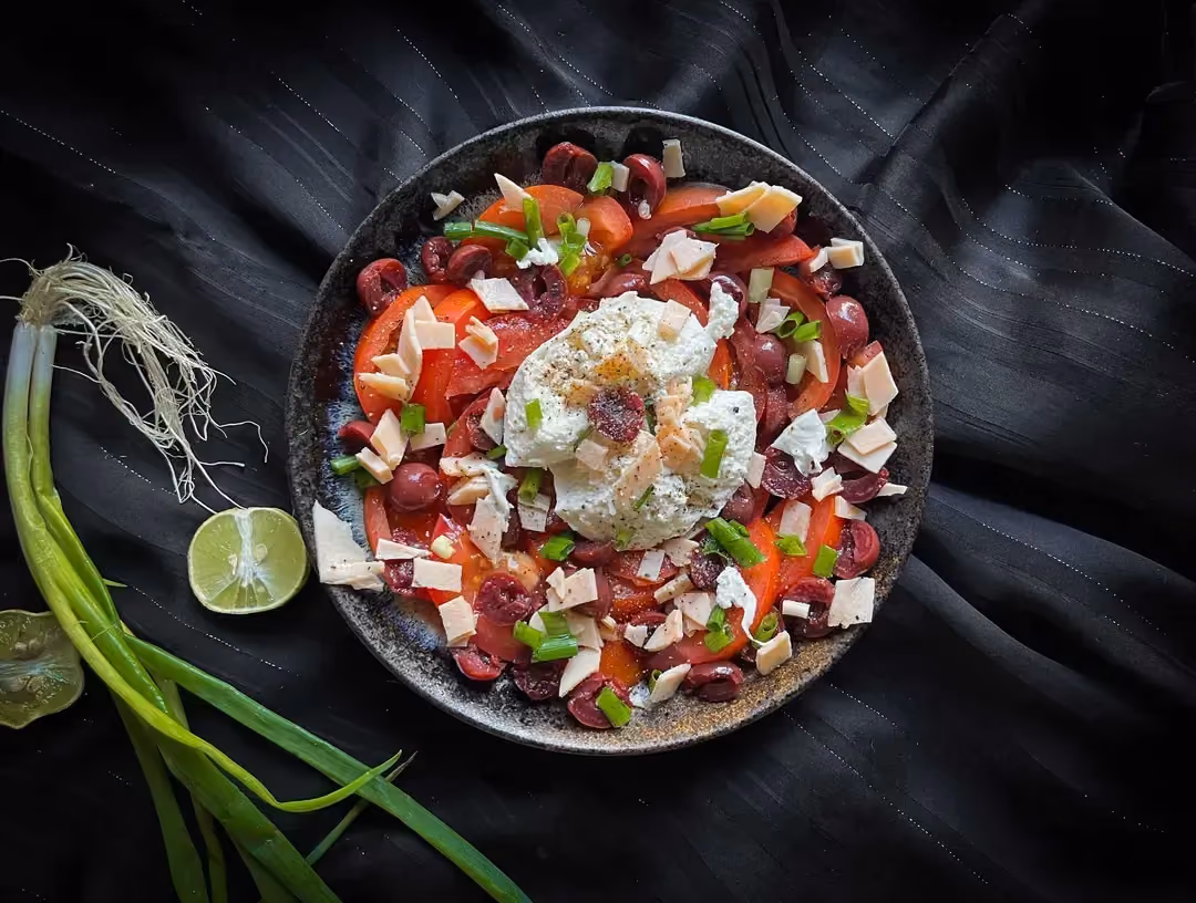 The cherry, tomato, turkey breast, and burrata salad is presented in a small salad bowl. A lemon cut in half and some onion are next to it.