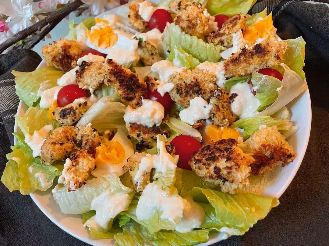 Cette salade César est composée de tomates cerises, d'oeufs, de sauce blanche, avec des morceaux de poulet panés et aussi de la Whey protéine.
