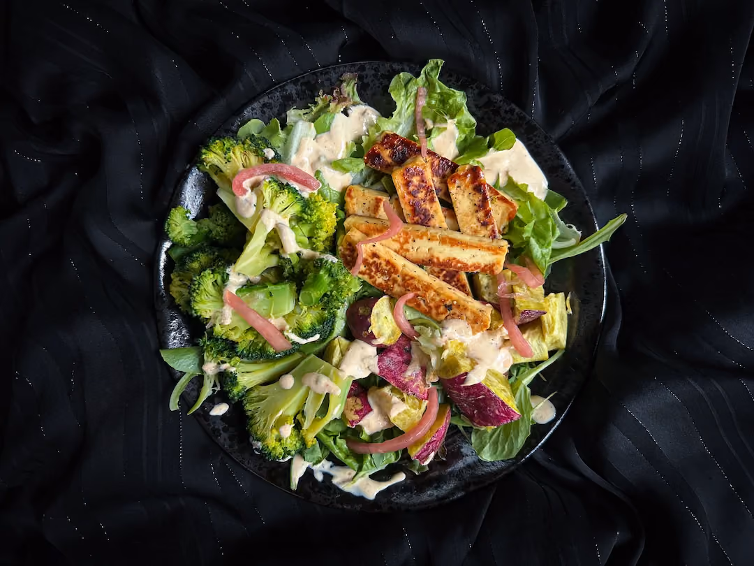The mixed salad with halloumi cheese grilled with maple syrup, sweet potatoes, broccoli, and red pesto is presented in a small salad bowl.