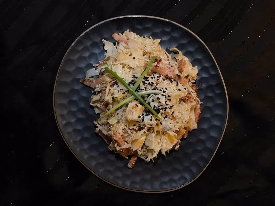 In a small blue salad bowl is a salad made with cabbage, bacon strips, and Comté cheese.