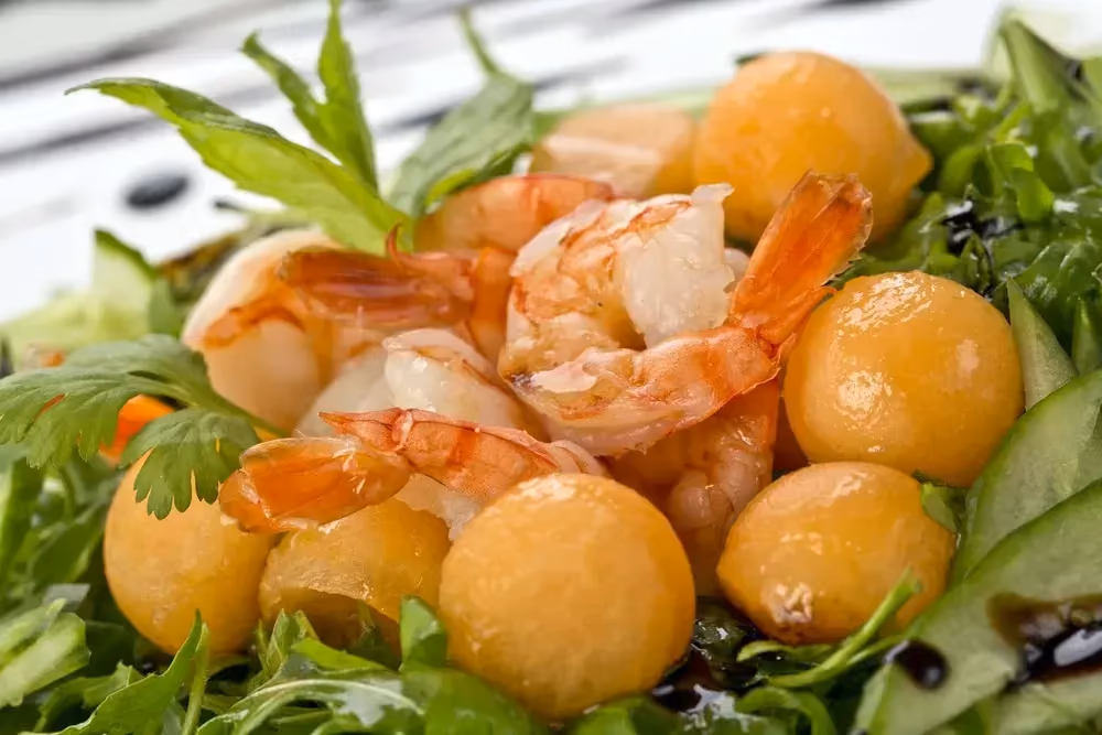 On a bed of fresh mint and cilantro leaves, there are shrimp and pretty melon balls making up this refreshing salad.
