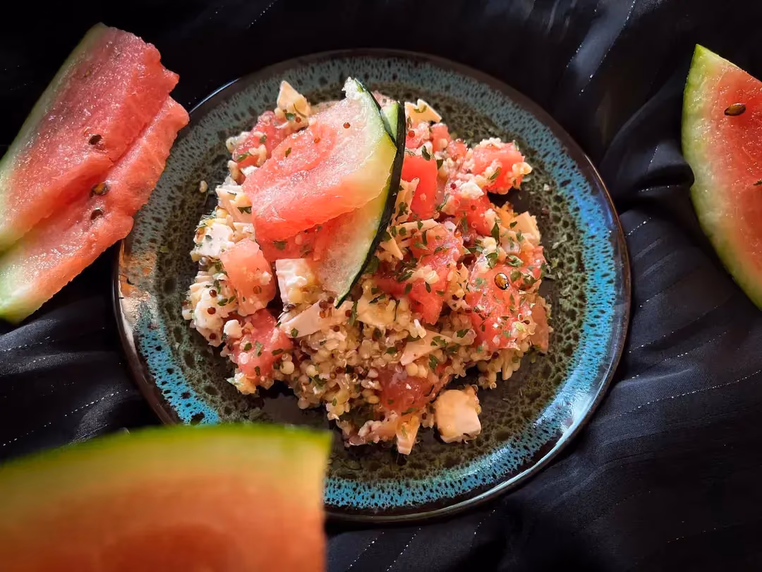 A small bowl holds this refreshing salad made with watermelon cut into large cubes, quinoa, feta, and turkey breast.